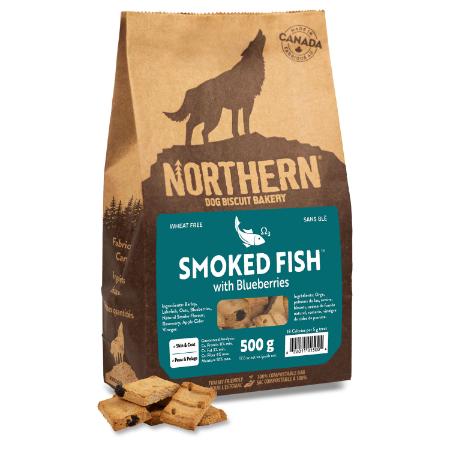 A brown bag of Northern Dog Biscuit Bakery treats, labeled "Smoked Fish with Blueberries," with images of a wolf silhouette and fish, and several square dog biscuits in front of the bag.