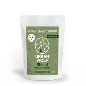 A white pouch labeled "Urban Wolf Shield" daily dog food topper, with green packaging highlighting it is natural, healthy, holistic, and chemical-free; designed to deter ticks and fleas.