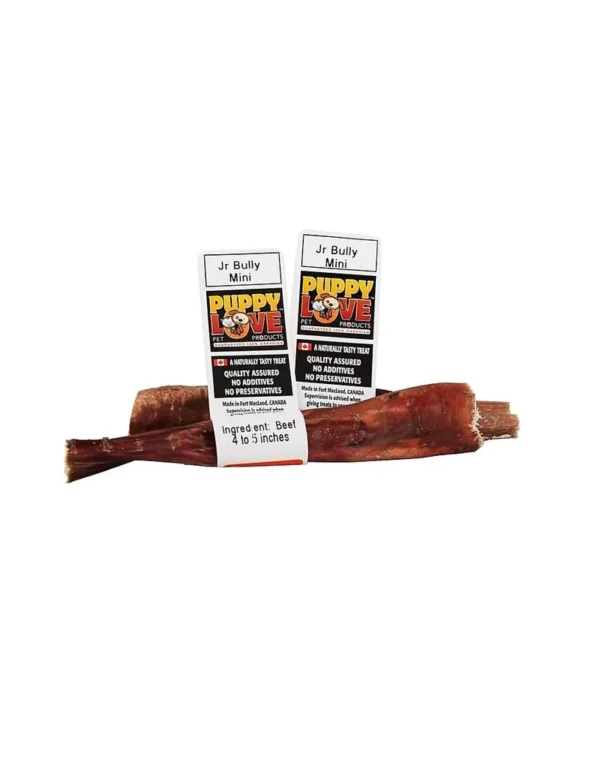 Two packages of Puppy Love Jr Bully Mini dog treats are displayed with a single long treat lying in front. The packaging highlights natural ingredients, quality assurance, and lack of preservatives.