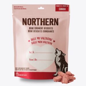 A pink bag of Northern Mini Crunchy Biscuits for dogs, featuring a wolf illustration, a heart with "Beef My Valentine!" text, and gift label fields for "To" and "From." Some heart-shaped biscuits are shown in front.