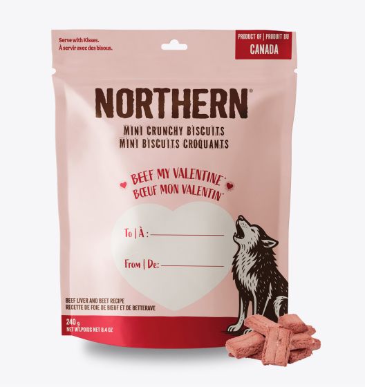 A pink bag of Northern Mini Crunchy Biscuits for dogs, featuring a wolf illustration, a heart with "Beef My Valentine!" text, and gift label fields for "To" and "From." Some heart-shaped biscuits are shown in front.