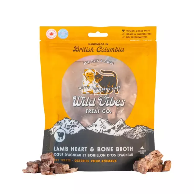 A package of Wild Vibes Treat Co. Lamb Heart & Bone Broth pet treats stands upright, displaying its orange and brown design with illustrations of a cat, dog, and mountains. Several pieces of the treats are placed in front.