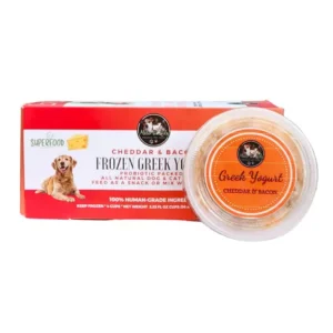 A red and white box labeled “Cheddar & Bacon Frozen Greek Yogurt” for dogs sits next to an open container of the yogurt. The packaging features a dog, cheese graphic, and notes it is made with all-natural, human-grade ingredients.