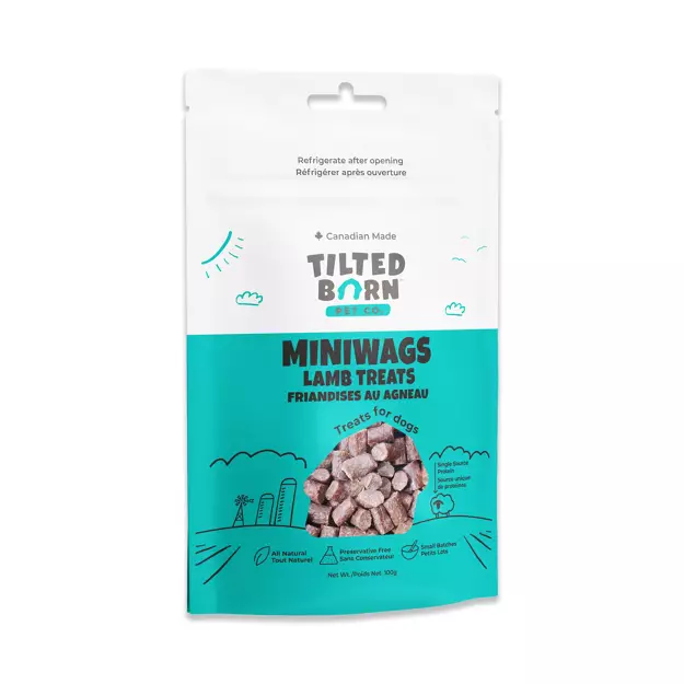 A white and teal resealable bag of Tilted Barn Miniwags Lamb Treats for dogs, featuring images of dog treats and illustrations of a barn, clouds, and grass. The bag states it is Canadian made and all natural.