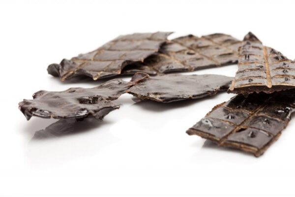 Close-up of dark brown dried seaweed chips arranged on a white surface. The chips have a glossy finish and are irregularly shaped, showcasing a textured appearance.