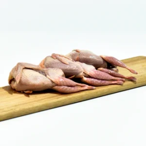 Four raw, whole quails are arranged on a wooden cutting board against a white background.