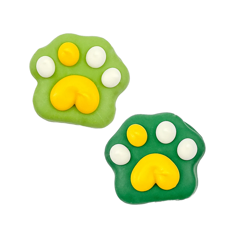 Two decorated cookies shaped like animal paw prints, one light green and the other dark green, both with yellow pads and white toes, on a transparent background.