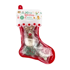 A festive dog treat stocking labeled "Merry Woofmas" with four holiday-themed treats shaped like a reindeer, Santa, tree, and bone. The treats are wrapped in clear plastic and the stocking is red with a decorative top.