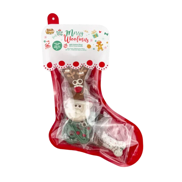 A festive dog treat stocking labeled "Merry Woofmas" with four holiday-themed treats shaped like a reindeer, Santa, tree, and bone. The treats are wrapped in clear plastic and the stocking is red with a decorative top.