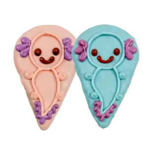 Two decorated cookies shaped like cute axolotls, one pink and one blue, each with a smiling face, red eyes, and purple gill details.