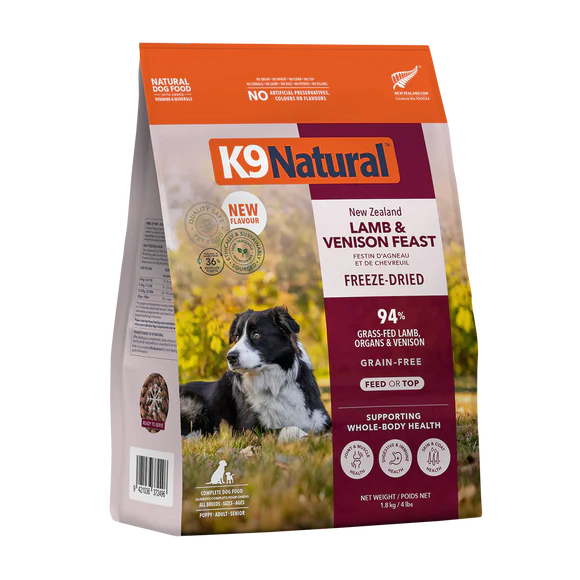A bag of K9 Natural freeze-dried dog food, Lamb & Venison Feast flavor, featuring a photo of a black and white dog lying on grass. The packaging highlights grain-free ingredients and whole-body health support.