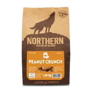 A brown bag of Northern Dog Biscuit Bakery Peanut Crunch dog treats, featuring a wolf silhouette and "Wheat Free" label. The bag weighs 1.36 kg and has a maple leaf and "Made in Canada" emblem.