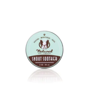 A tin of Snout Soother from Natural Dog Company, 2 oz (59 mL), is shown. The label is light green and brown with an illustration of a dog. It includes the words "Sooth. Moisturize. Heal.