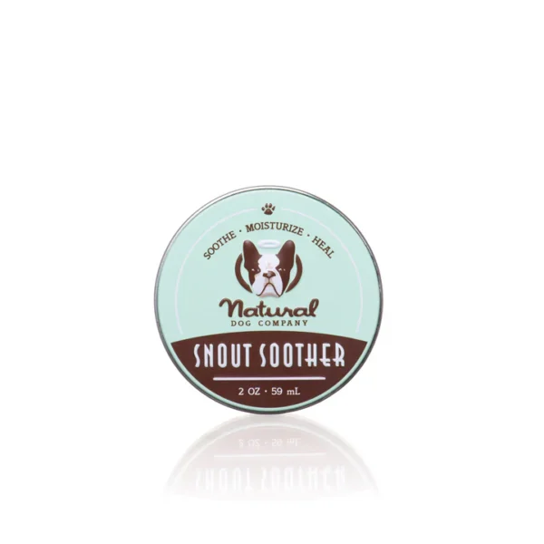 A tin of Snout Soother from Natural Dog Company, 2 oz (59 mL), is shown. The label is light green and brown with an illustration of a dog. It includes the words "Sooth. Moisturize. Heal.