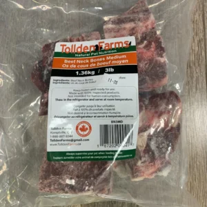 A 1.36 kg (3 lb) clear plastic bag of Tollden Farms Beef Neck Small for pets rests on a wooden surface, featuring a label in English and French with ingredients and company details.