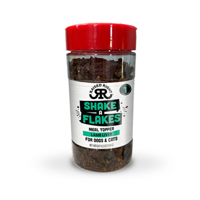 A clear plastic container with a red lid labeled "Shake A Flakes Meal Topper Lamb Liver for Dogs & Cats" by Raised Right, showing dried lamb liver pieces inside.
