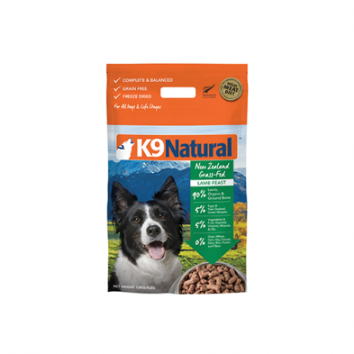 A package of K9 Natural dog food with a picture of a black and white dog. The bag is labeled "New Zealand Grass-Fed Lamb Feast" and mentions being grain-free and freeze-dried. A scenic mountain background is visible on the package.