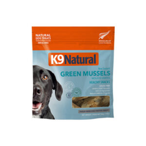 A bag of K9 Natural Green Mussels dog treats, featuring an image of a happy black dog on the left and a clear window showing the treats inside. The packaging is blue and orange.