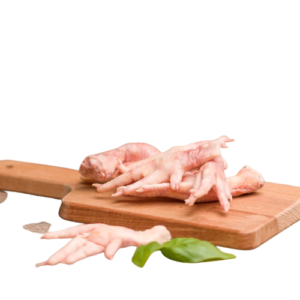 A wooden cutting board with several raw chicken feet stacked on it. In front of the board, there are a few more chicken feet and a sprig of fresh green leaves. The background is plain and out of focus.