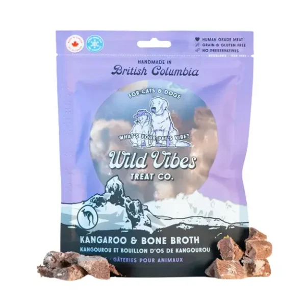 A package of Wild Vibes Treat Co. Kangaroo & Bone Broth pet treats for cats and dogs, with small chunks of the treat placed beside the bag. The packaging is purple and blue with illustrated animals.