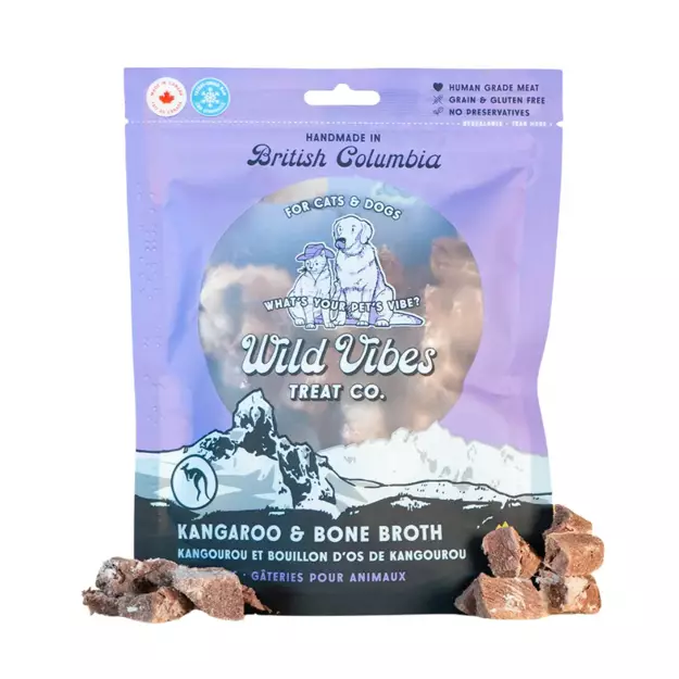 A package of Wild Vibes Treat Co. Kangaroo & Bone Broth pet treats for cats and dogs, with small chunks of the treat placed beside the bag. The packaging is purple and blue with illustrated animals.