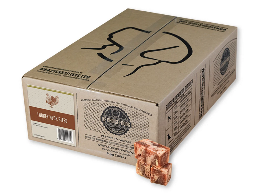 A cardboard box labeled "Turkey Neck Bites" from K9 Choice Foods sits on a white surface, with three frozen, cube-shaped pieces of turkey neck placed in front of it.