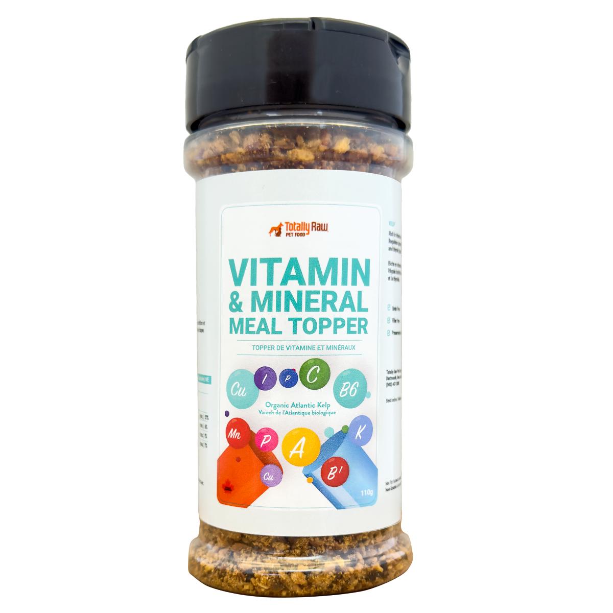 A clear plastic container of Totally Raw Vitamin & Mineral Meal Topper for pets, with a black lid and a white label listing vitamins and minerals. The contents are visible through the container.
