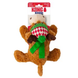 Plush dog toy shaped like a moose wearing a green scarf and red-green knit hat, labeled "KONG Cozie." The toy is brown with light brown antlers and has a festive appearance.