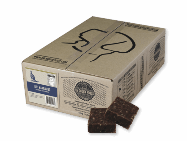 A cardboard box labeled "K9 Choice Kangaroo 20 lb" features black line art of a dog's head, nutrition facts, and a "Just Kangaroo" label. Two brown, square meat patties sit in front of the box.