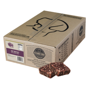 A cardboard box of K9 Choice Foods with a buffalo illustration on it. The label reads "Just Buffalo." Two pieces of raw buffalo meat are placed in front of the box.