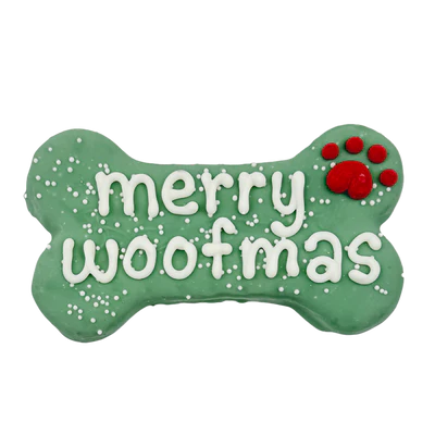 A green bone-shaped dog treat with white icing reading "merry woofmas" and a red paw print in the upper right corner, decorated with small white sprinkles.