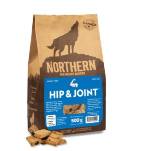 A brown paper bag of Northern Dog Biscuit Bakery Hip & Joint dog treats, featuring a wolf silhouette and a blue label. Some square treats are scattered in front of the bag. The bag states "Wheat Free" and "Made in Canada.