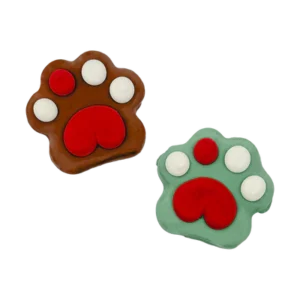 Two paw-shaped cookies are decorated with icing. One is brown with white toes and a red paw pad, while the other is green with similar decoration. Both have a playful, cartoon-like appearance.