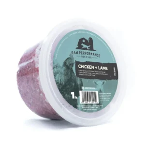 A 1-pound tub of Raw Performance Dog Food, Chicken + Lamb blend, with a translucent lid and a green label featuring a chicken illustration and product details. The food inside is visibly ground and reddish in color.