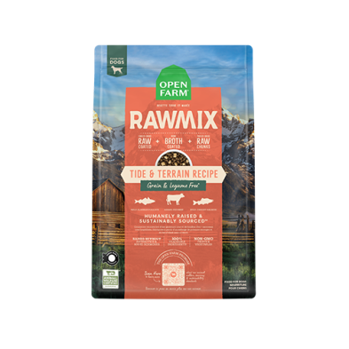 A bag of Open Farm RawMix dog food, Tide & Terrain Recipe. Features raw and broth-coated clusters. Highlights grain and legume-free ingredients, humanely raised and sustainably sourced, set against a backdrop of mountains and a wooden cabin.