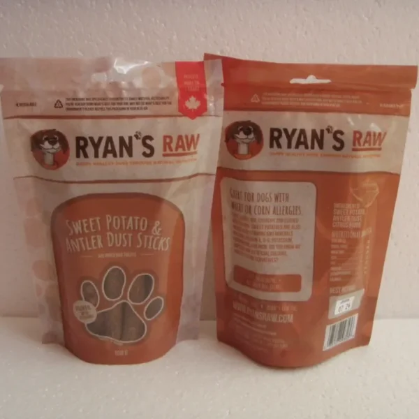 Two bags of "RYAN'S RAW" dog treats are displayed. The front bag features "Sweet Potato & Antler Dust Sticks" with a paw-shaped design. The back bag shows the ingredients and details, emphasizing that the product is great for dogs with wheat or corn allergies.