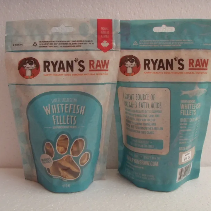Two teal and white pouches of Ryan’s Raw Dehydrated Whitefish Fillets 110 g are shown; one displays the front label with a paw print window, and the other shows the back with nutritional information.