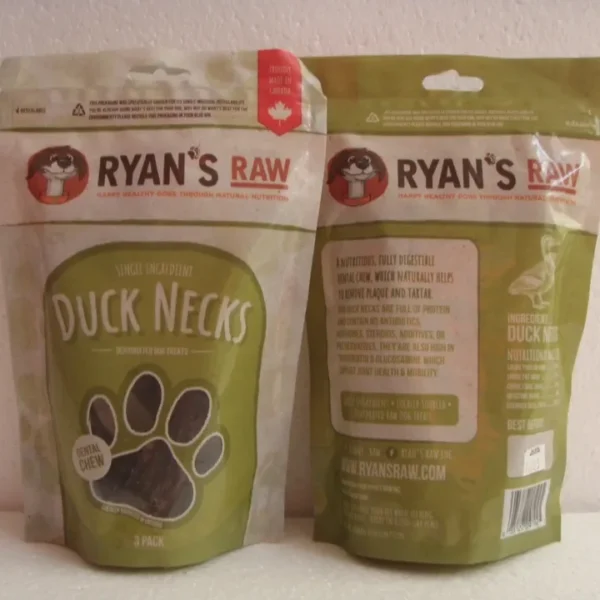 Two green and beige pouches of Ryan's Raw Duck Necks for dogs are shown. One pouch displays the front label; the other shows the back with product details and branding. Both feature a paw print and cartoon dog logo.