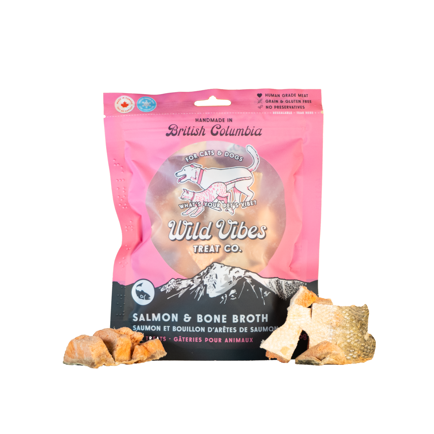A pink bag of Wild Vibes Treat Co. Salmon & Bone Broth pet treats for cats and dogs, with pieces of dried treat in front of the package. The bag features a mountain design and a dog illustration.